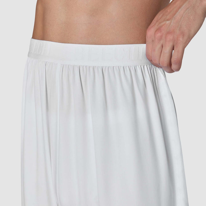 Close-up of a person wearing white satin or silky shorts, showing the elastic waistband and gathered fabric, with a hand pulling the side of the waistband.